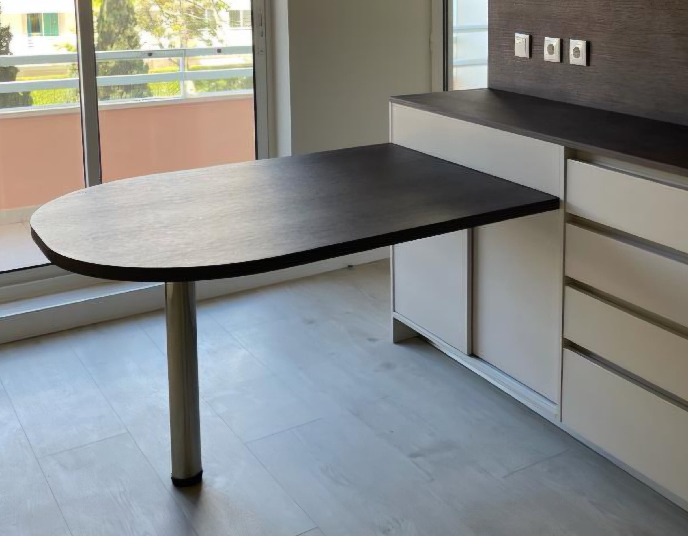Table en demi-lune en bois foncé sur pied en métal brossé, accolée au buffet à tiroirs et portes coulissantes
