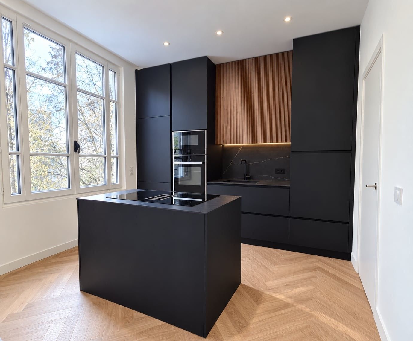 Îlot noir mat avec plaque de cuisson, devant les colonnes et les fours encastrés, sur parquet en point de Hongrie
