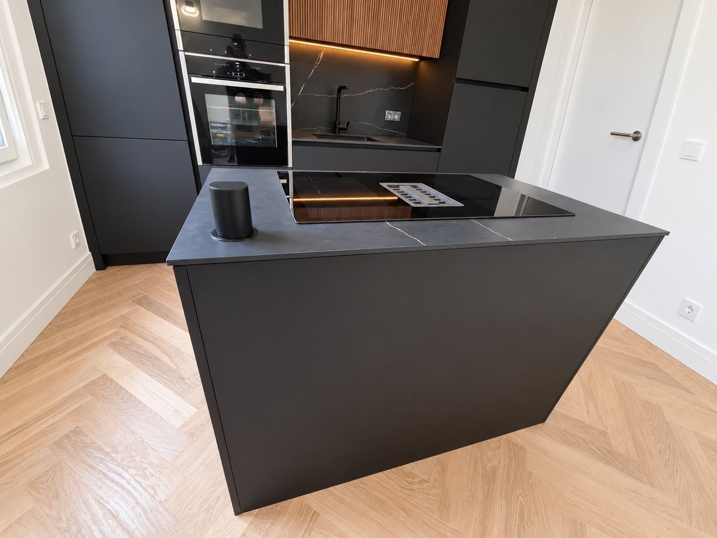 Plateau de l'îlot noir veiné avec plaque de cuisson à aspiration intégrée, face aux fours encastrés