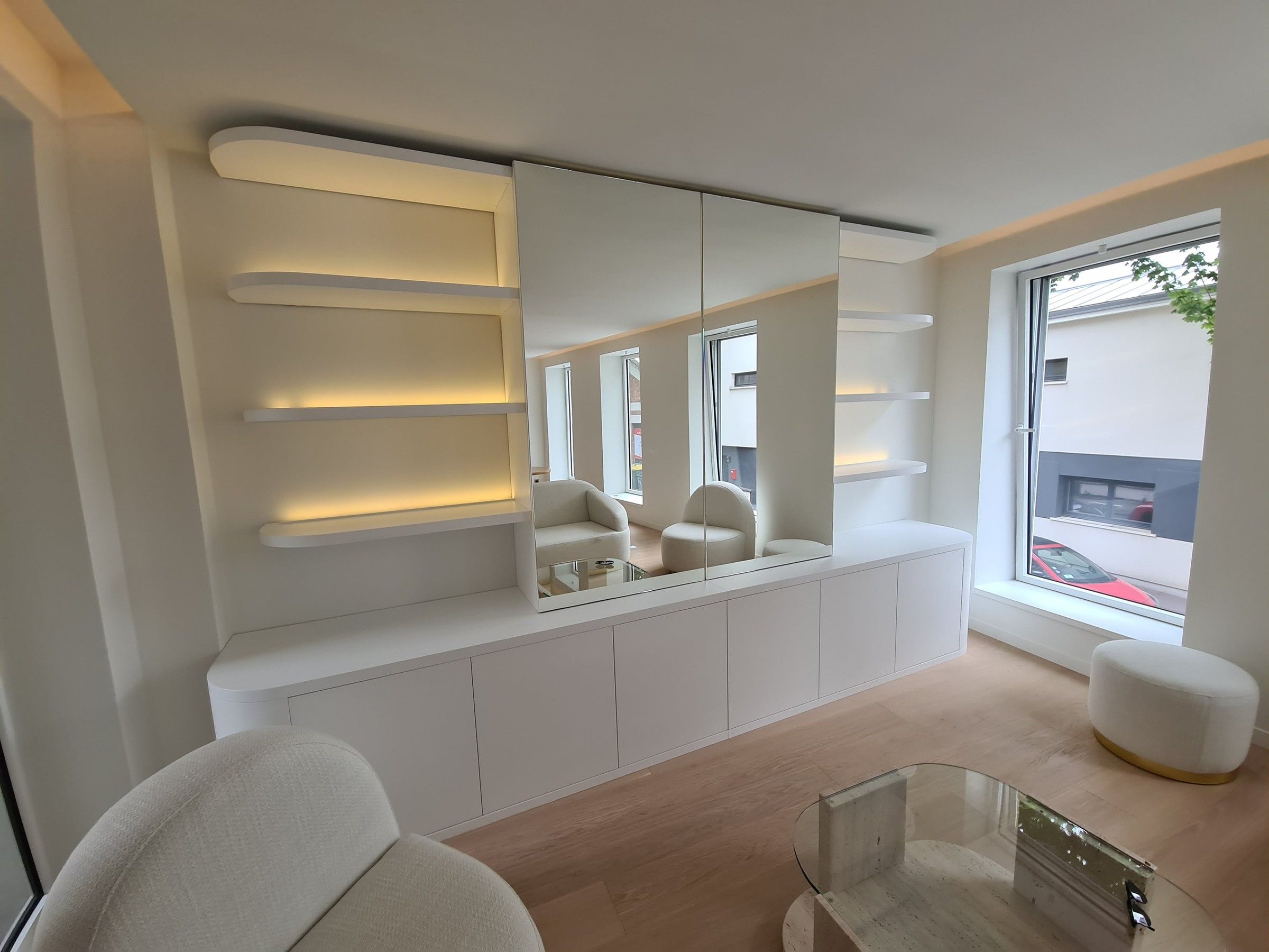 Meuble bas blanc aux angles cintrés, étagères rétroéclairées et grand miroir central