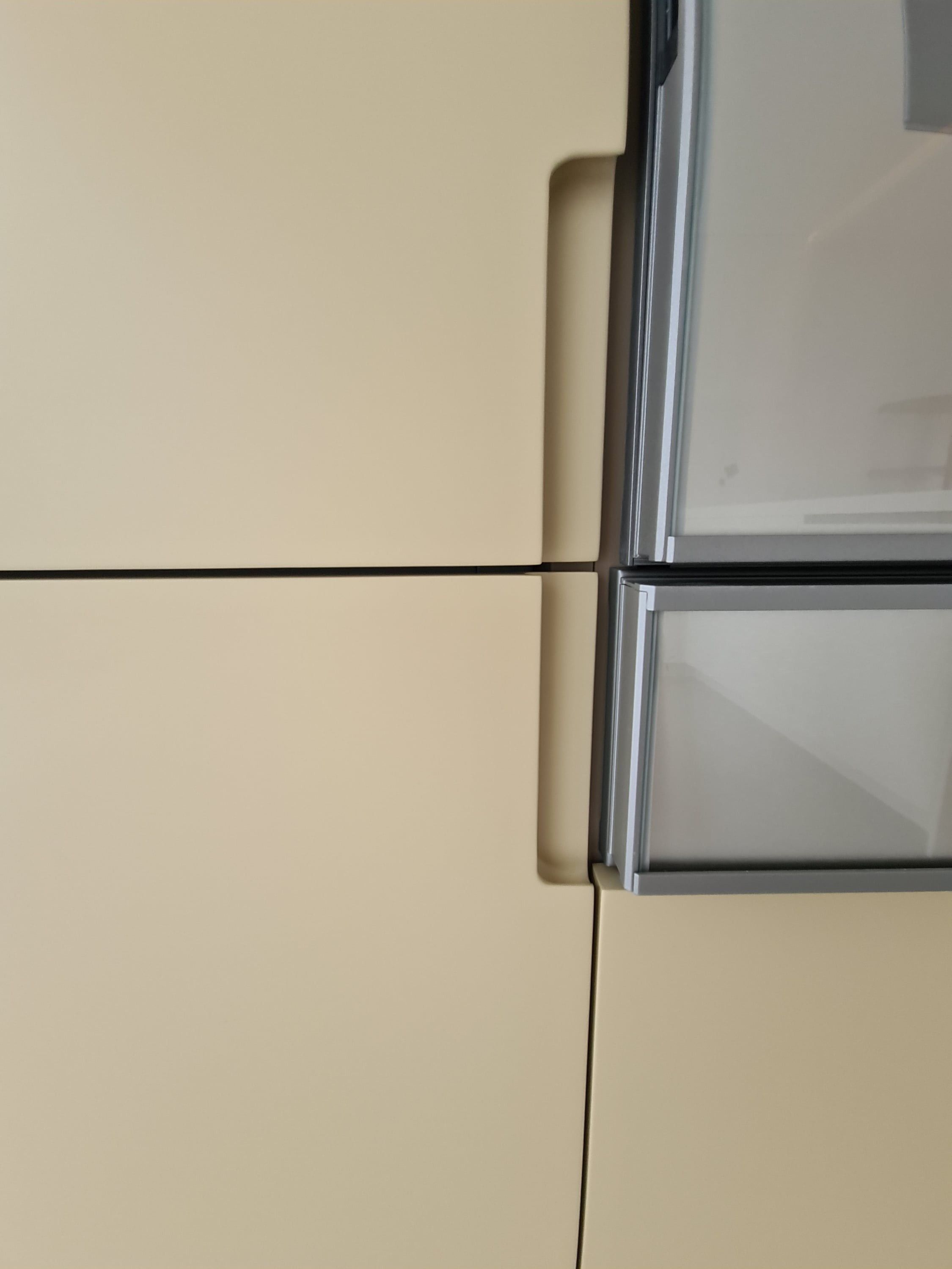 Détail d'une prise de main creusée dans une porte laquée sable, à côté d'un four