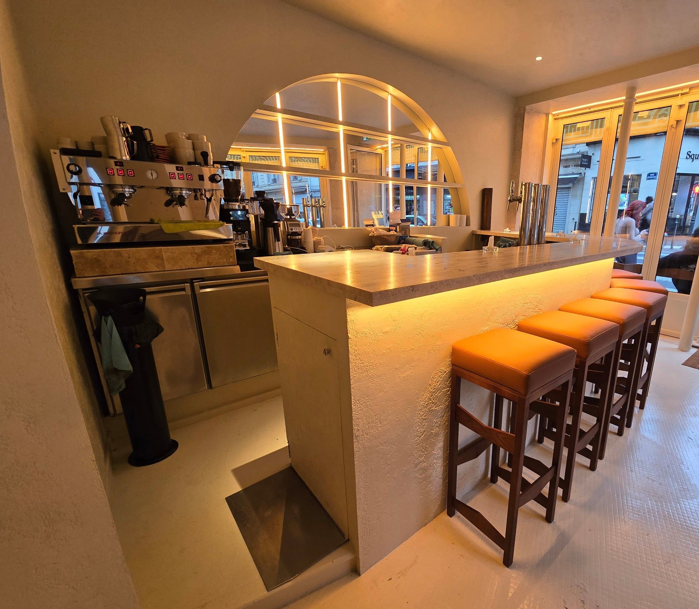 Côté service du bar, avec le poste café, le plateau en pierre éclairé en dessous et les tabourets alignés