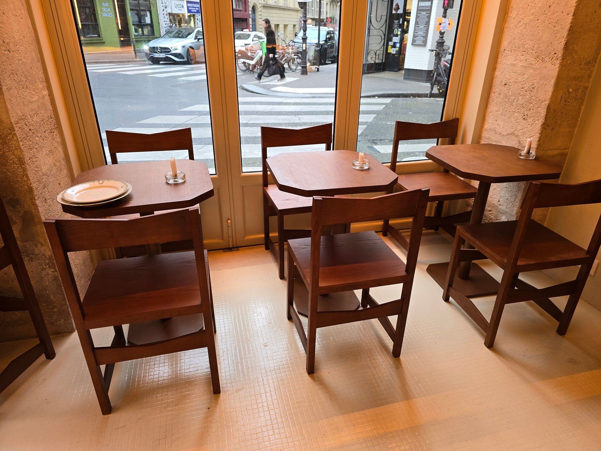 Tables à plateau à pans coupés et chaises en bois teinté devant les vitrines donnant sur la rue