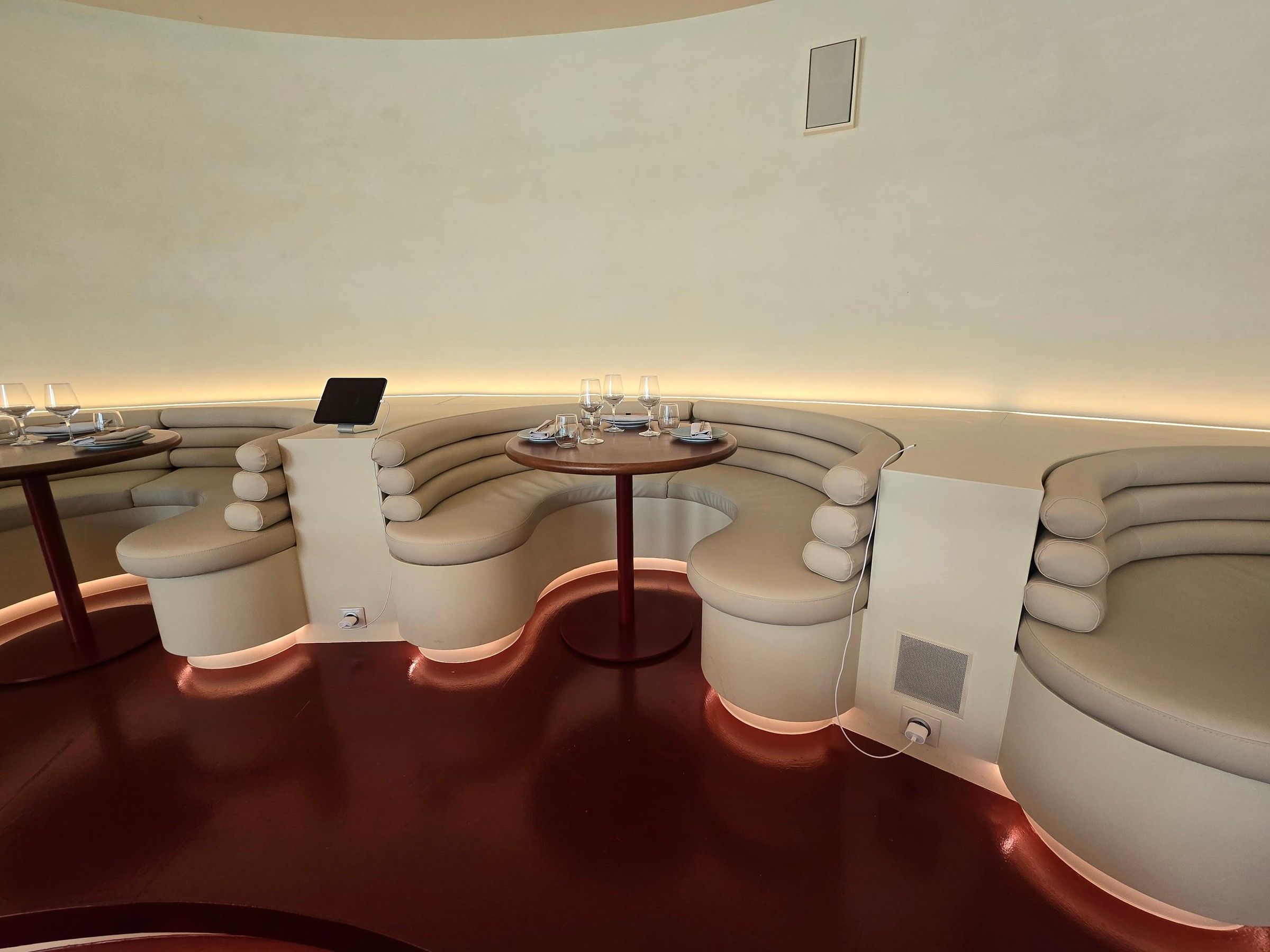 Banquettes crème en vague le long du mur, avec tables rondes sur pied rouge