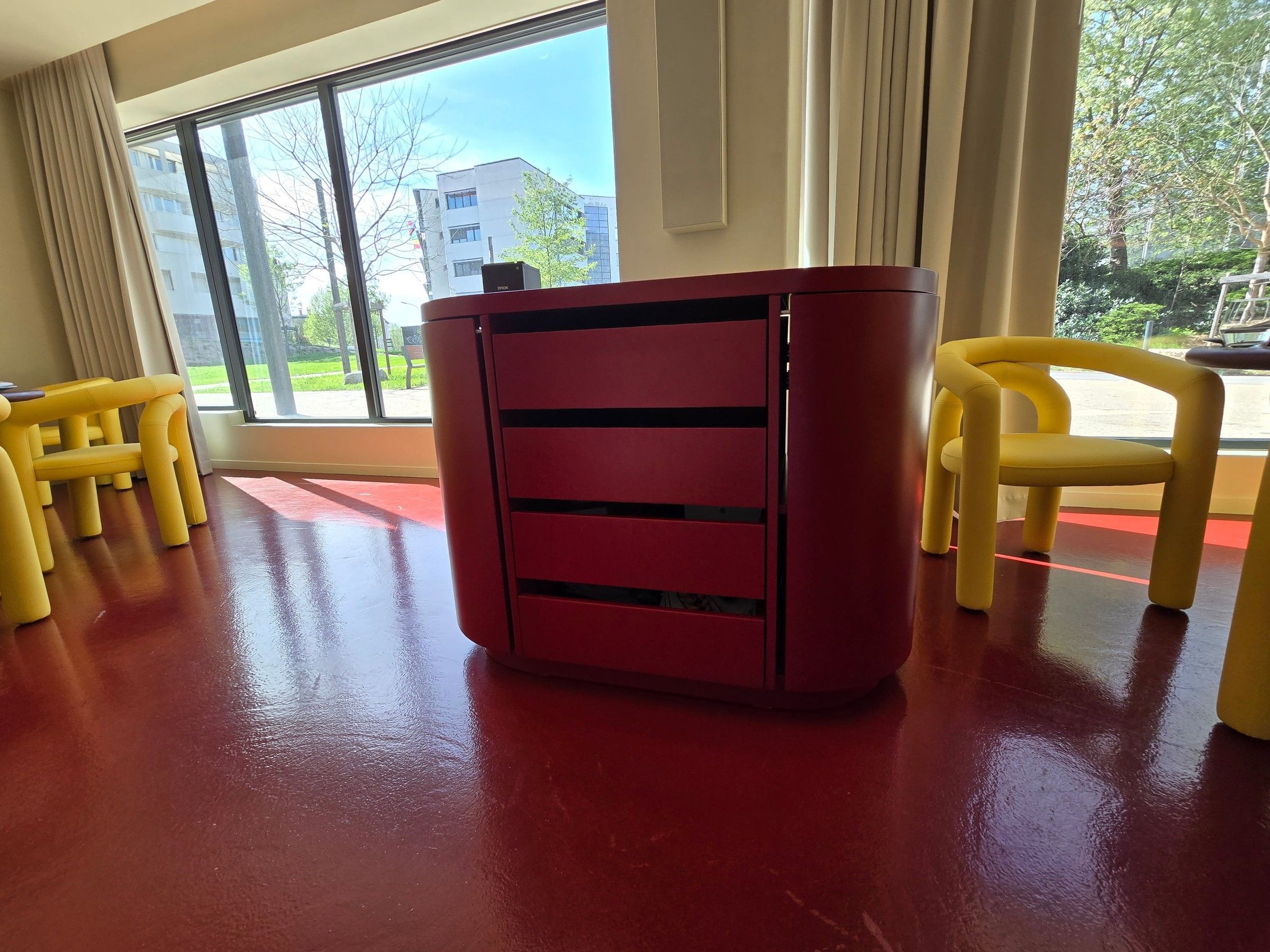 Meuble de service rouge à tiroirs, aux angles arrondis, entre deux fauteuils jaunes