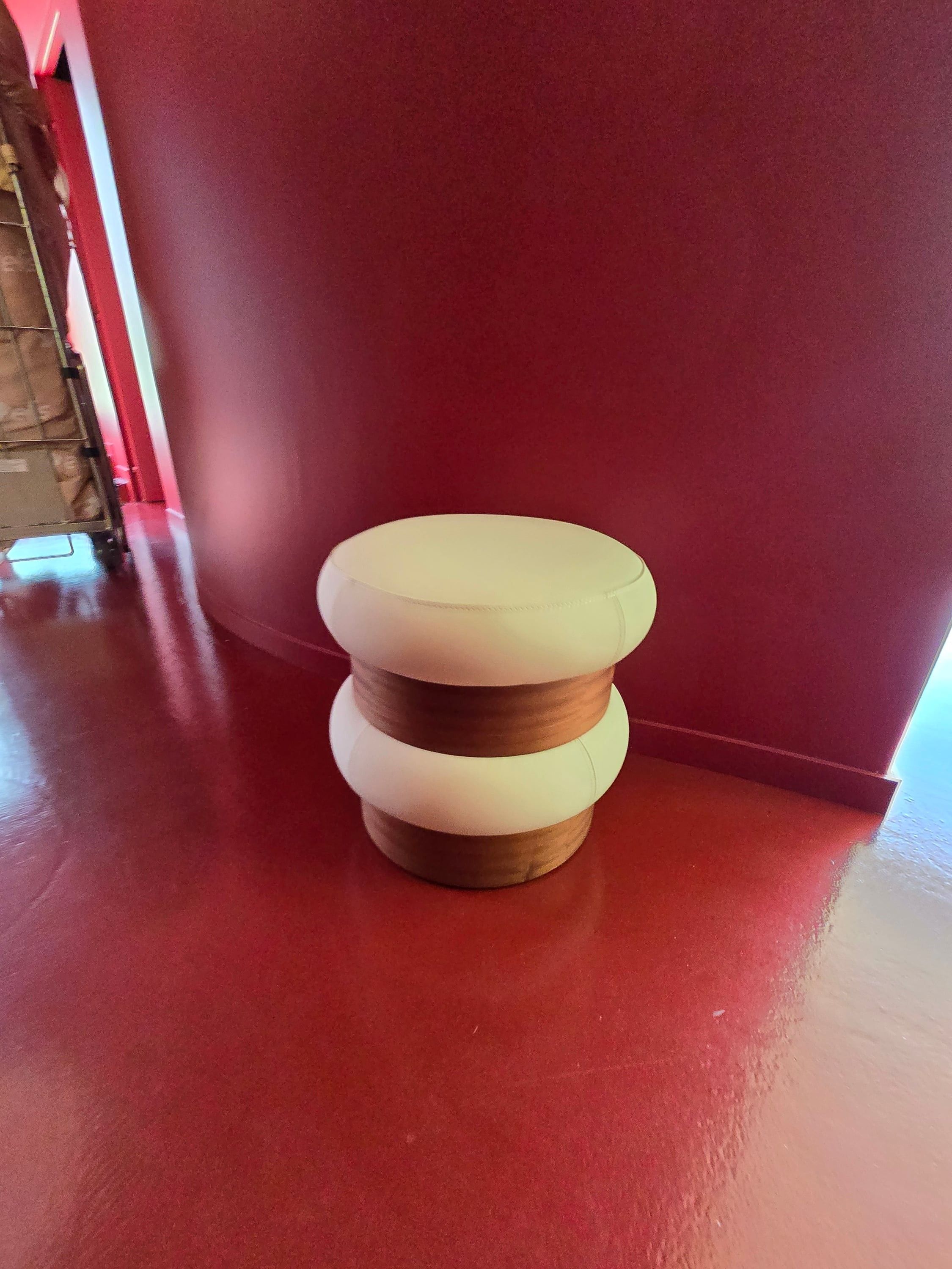 Pouf rond bicolore, crème et bois, au pied d'un mur rouge