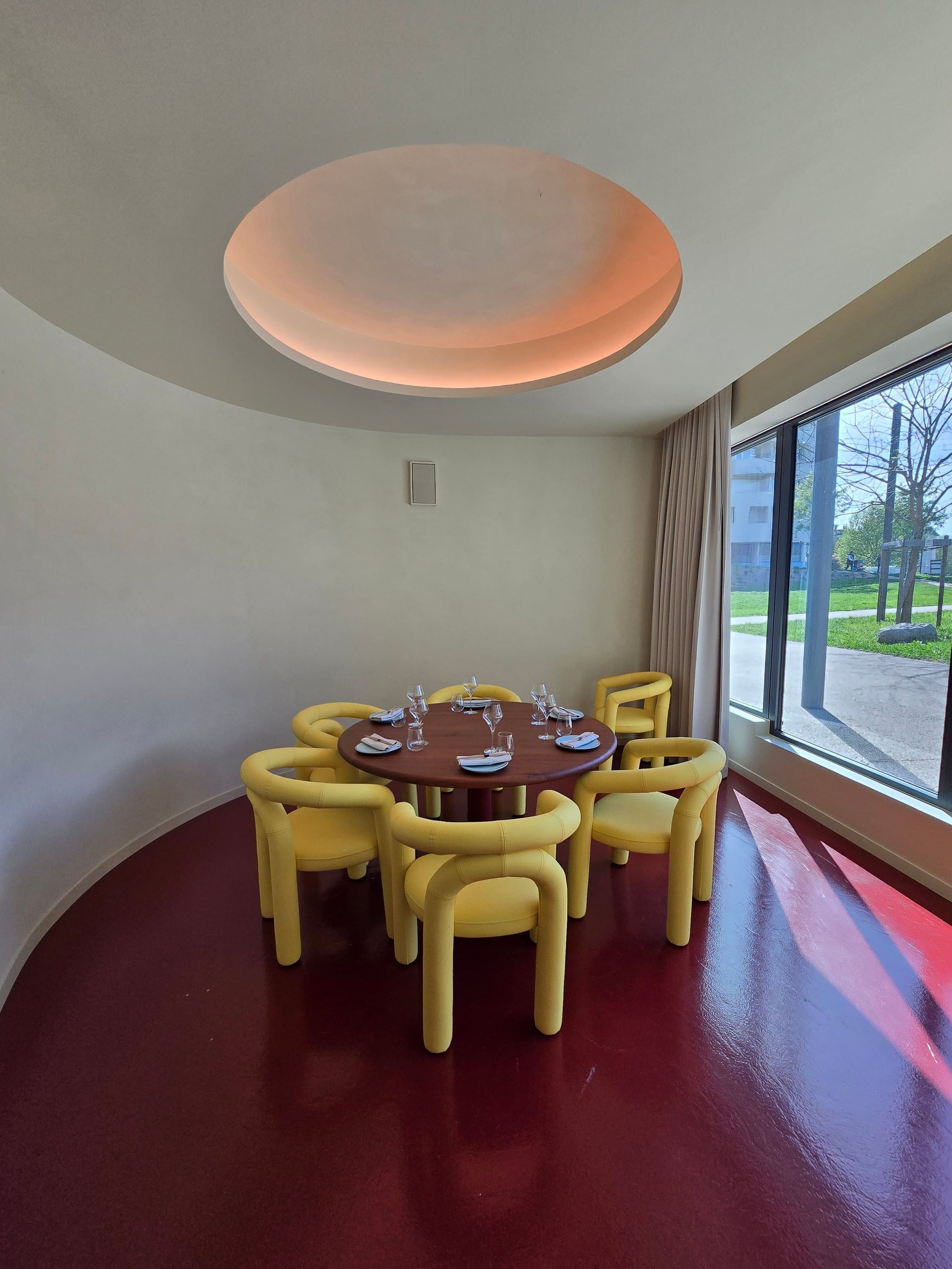 Table ronde et fauteuils jaunes près de la baie vitrée, sous un plafond en coupole éclairé